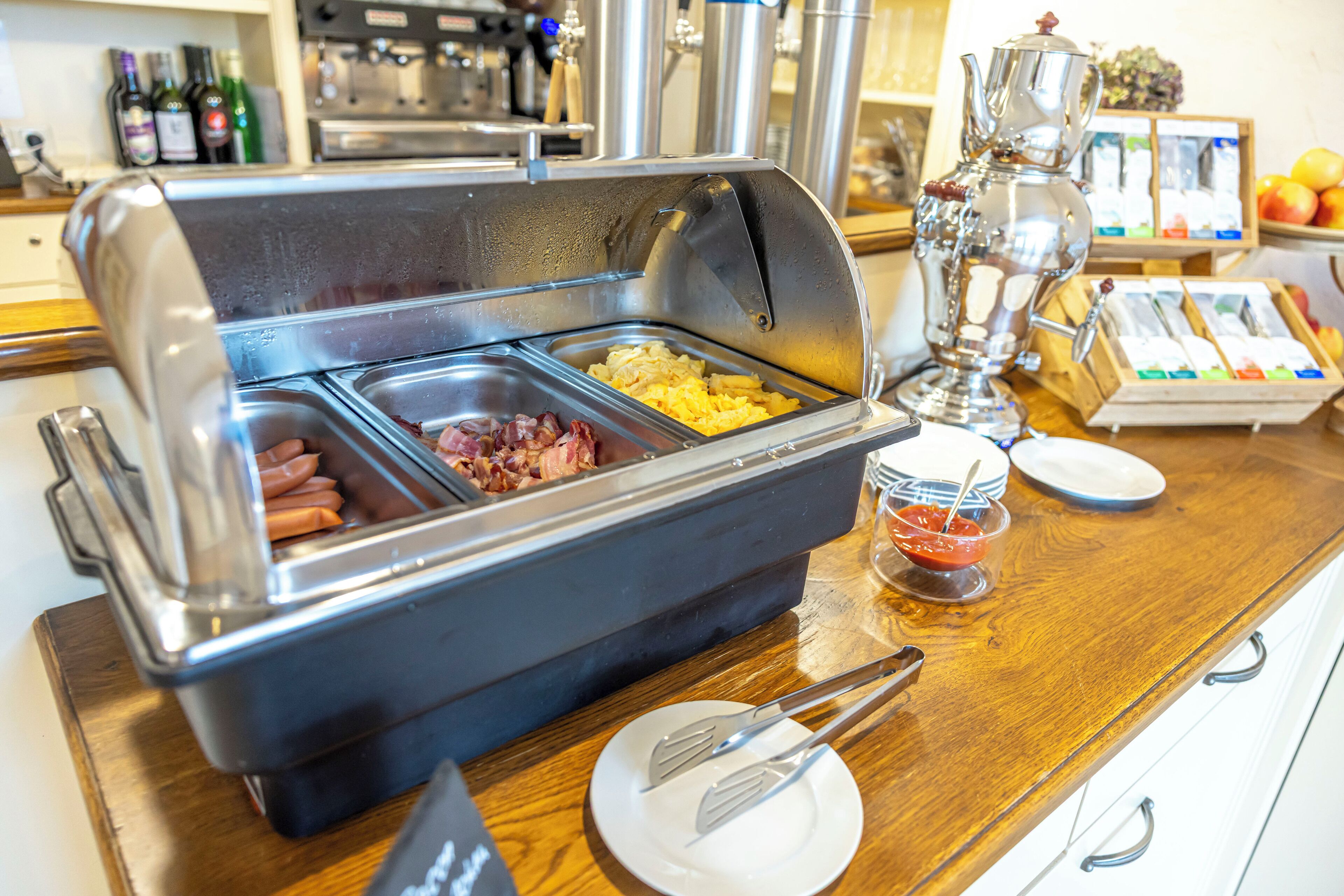 A buffet with various food options including hot dogs, eggs, and bacon.