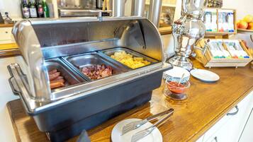 Buffet variado con opciones de comida que incluyen hot dogs, huevos y tocino.