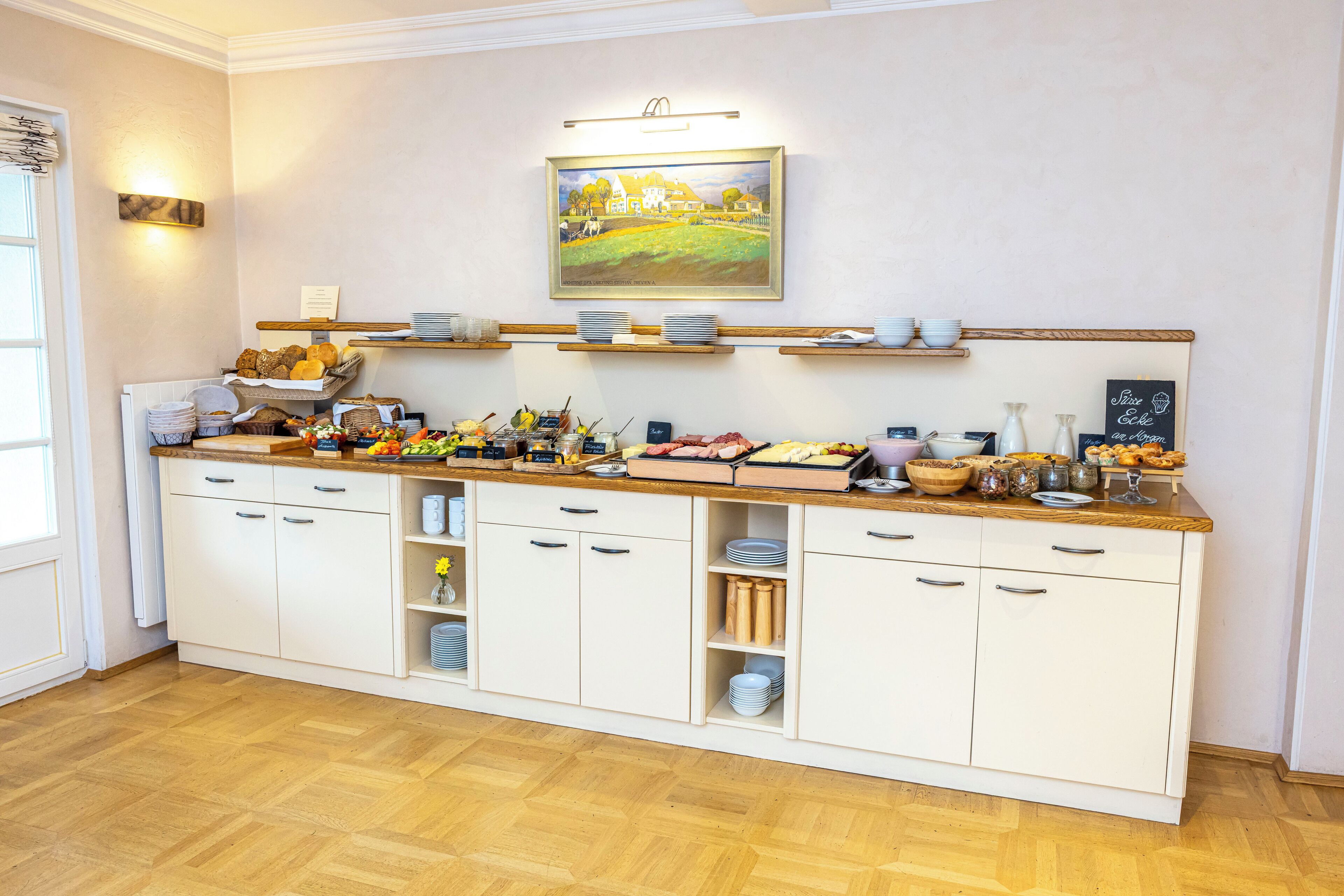A kitchen with white cabinets, wooden countertops, and a painting on the wall.