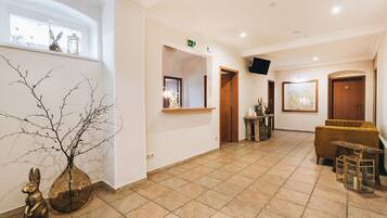 A spacious lobby with a tiled floor, a reception desk, a sofa, and a wall-mounted TV.