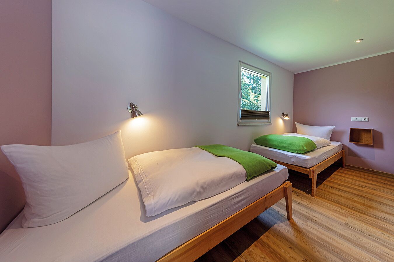 A bedroom with two beds, a window, and a wall-mounted light fixture.