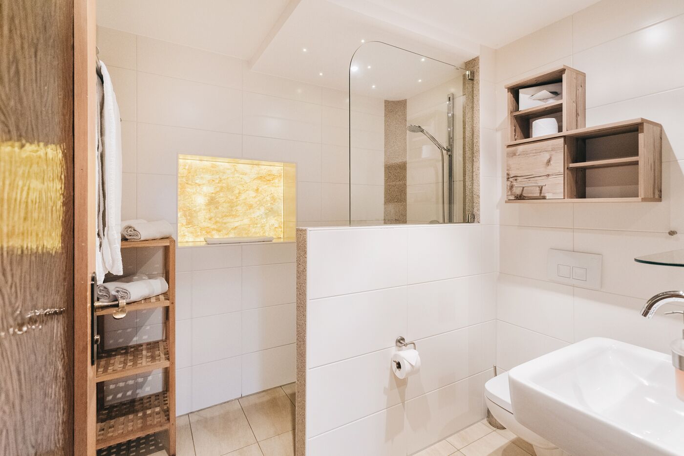 A modern bathroom with a glass shower enclosure, a white sink, and a wooden vanity with shelves.