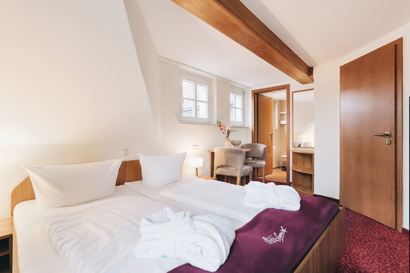 A hotel room with a bed, a chair, a desk, and a door.