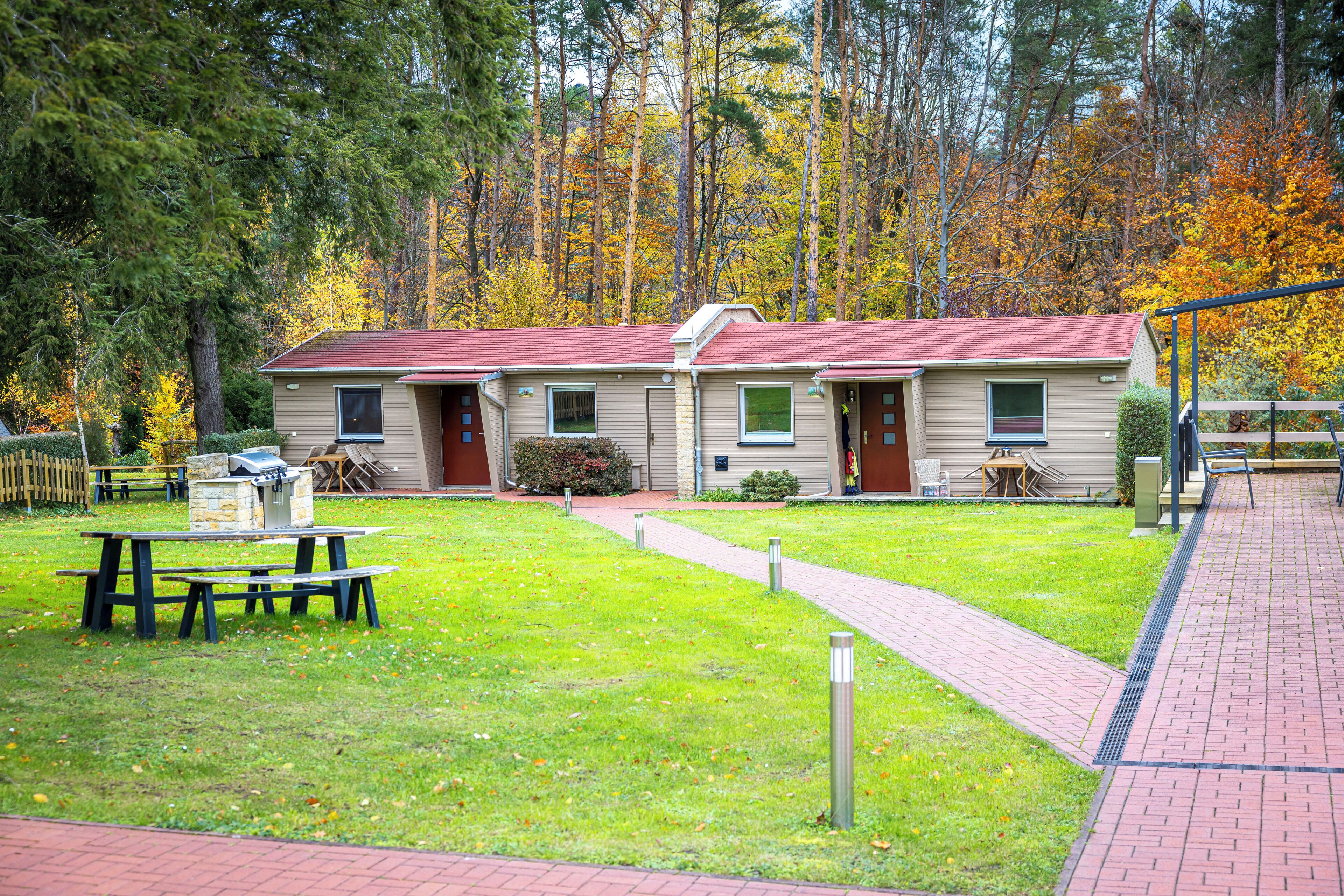 Een gebouw met twee verdiepingen, voorzien van een rood dak, een geplaveid pad en een picknicktafel op de voorgrond.