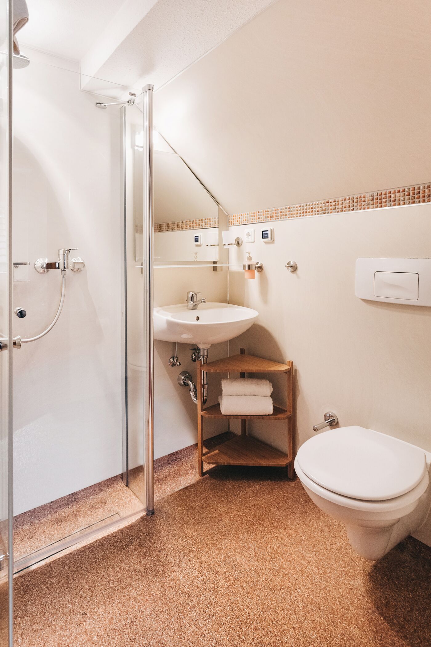 Ein Badezimmer mit Duschkabine aus Glas, einem Waschbecken, einer Toilette und einem hölzernen Ablagebereich mit Handtüchern.