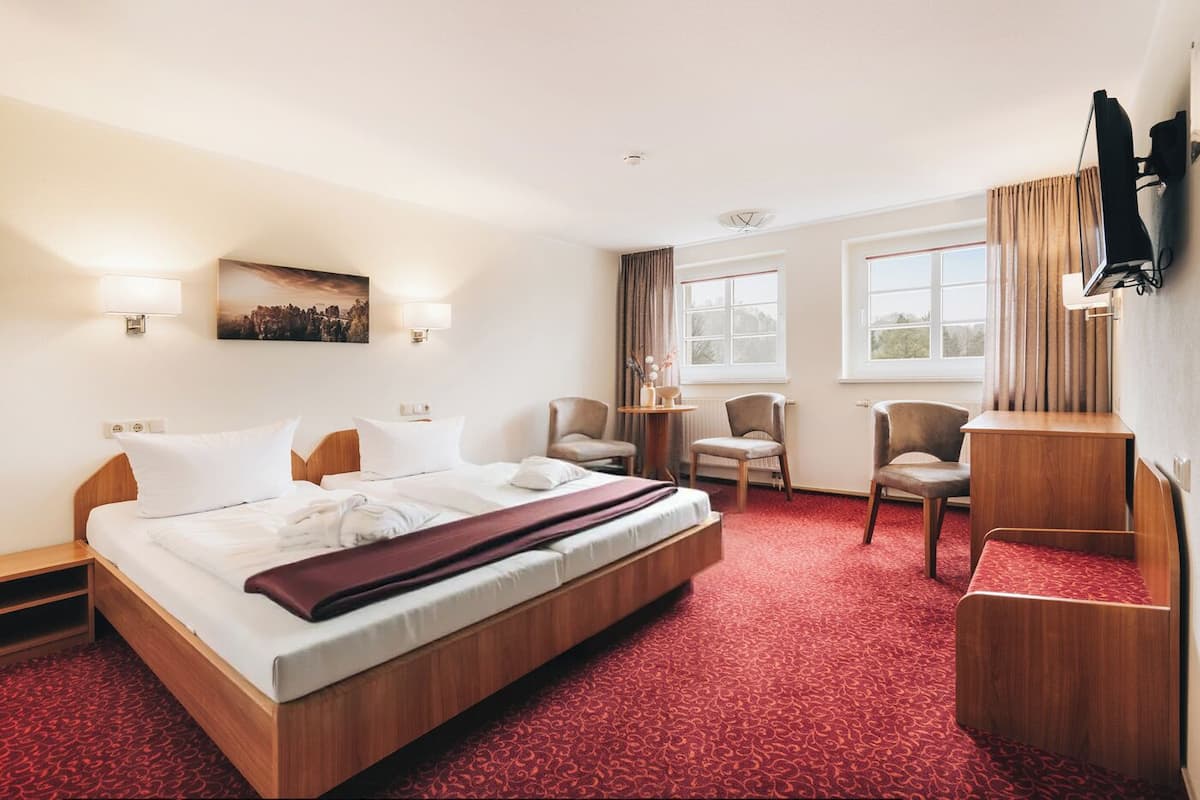 Une chambre d’hôtel avec un grand lit, deux chaises, une petite table et un téléviseur fixé au mur.