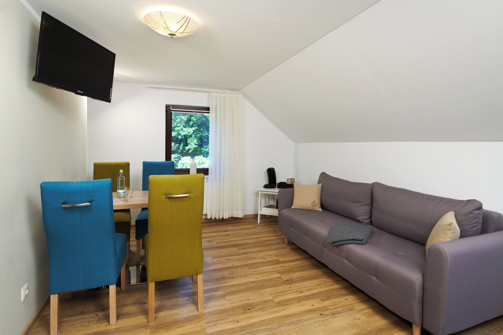 Un salon moderne comprenant un canapé, deux fauteuils, une table à manger et un téléviseur fixé au mur.
