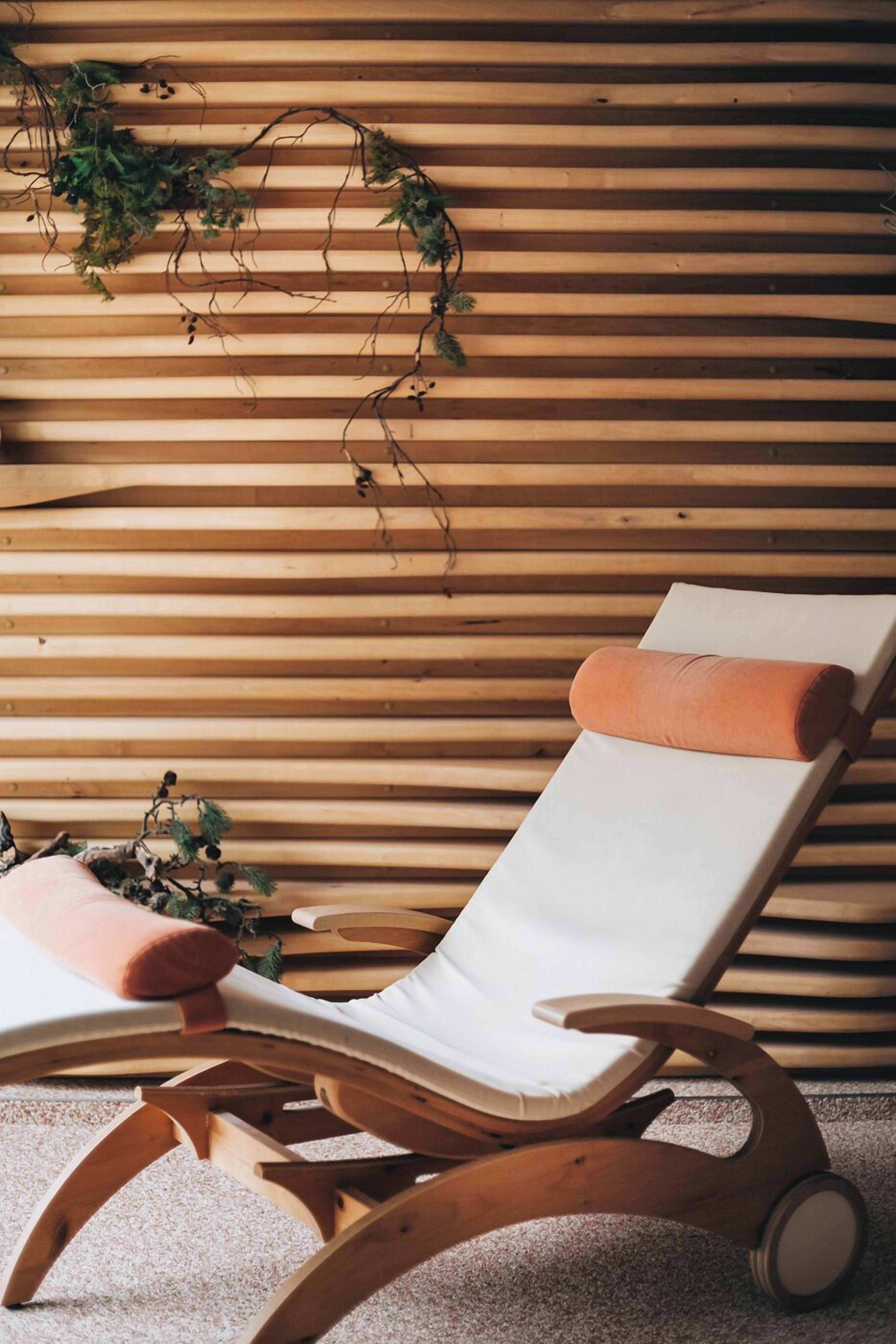 A wooden slatted wall with a white cushioned lounge chair and a small plant.