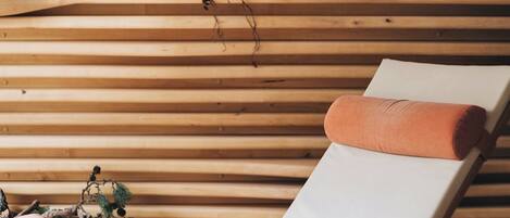 A wooden slatted wall with a white cushioned lounge chair and a small plant.