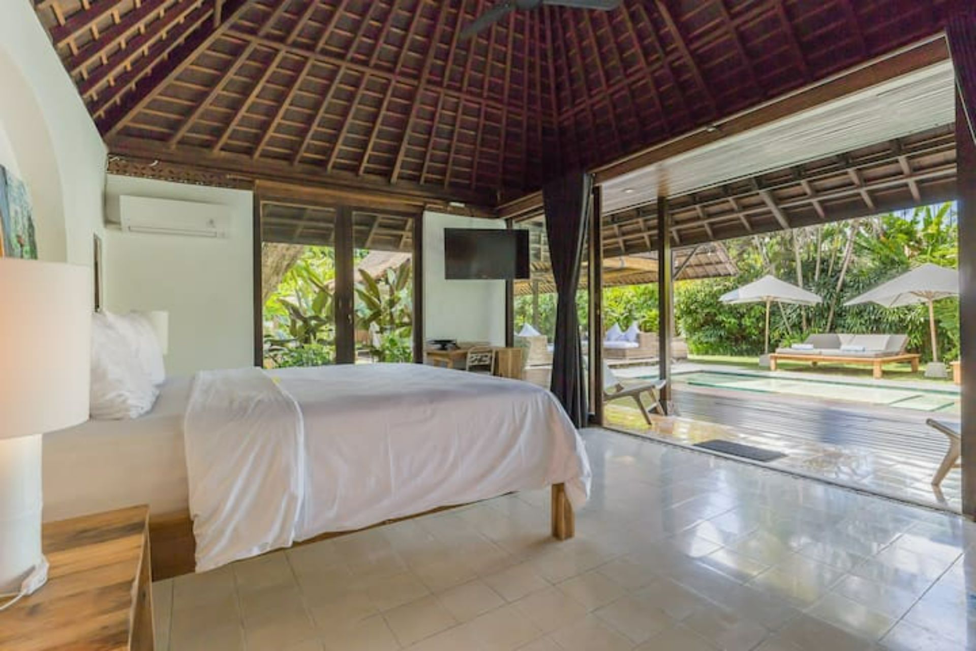 A bedroom with a bed, a TV, and a view of an outdoor pool area.