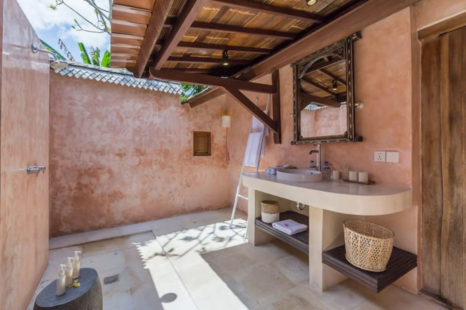 A bathroom with a wooden ceiling, a large mirror, a sink, and a small shelf with toiletries.