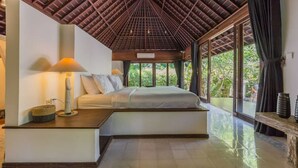 Ein Schlafzimmer mit Bett, Nachttisch, Lampe und Blick auf Grünanlagen durch große Fenster.