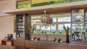A modern kitchen with a stone backsplash, a bar area with glassware, and a view of the outdoors. - Villa De Claris, Brand New Villa (Uvita)