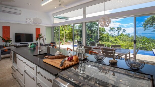 A modern kitchen with a large island, a built-in oven, and a view of the outdoors. - Villa De Claris, Brand New Villa (Uvita)