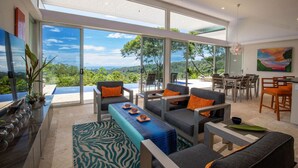 A modern living room with a large glass door leading to a balcony, offering a scenic view of the landscape. - Villa De Claris, Brand New Villa (Uvita)