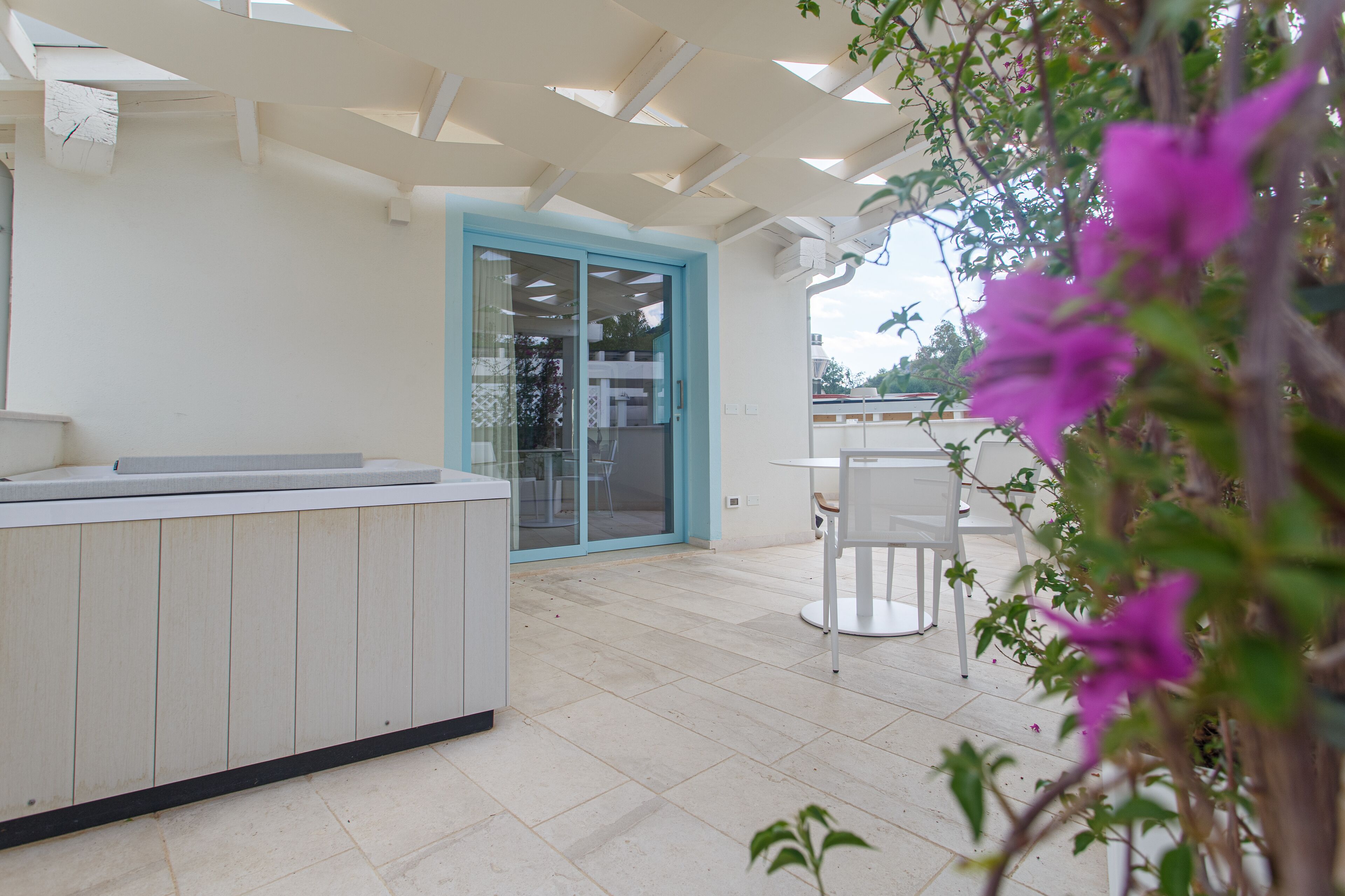 A modern outdoor patio with a white countertop, a glass door leading to an interior space, and a table with chairs.