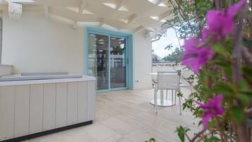 A modern outdoor patio with a white countertop, a glass door leading to an interior space, and a table with chairs.