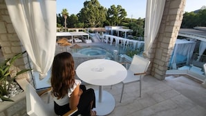 A woman sitting at a table on a balcony overlooking a pool area with outdoor seating and a hot tub. - Oasi Blu Sardinia (Pula)