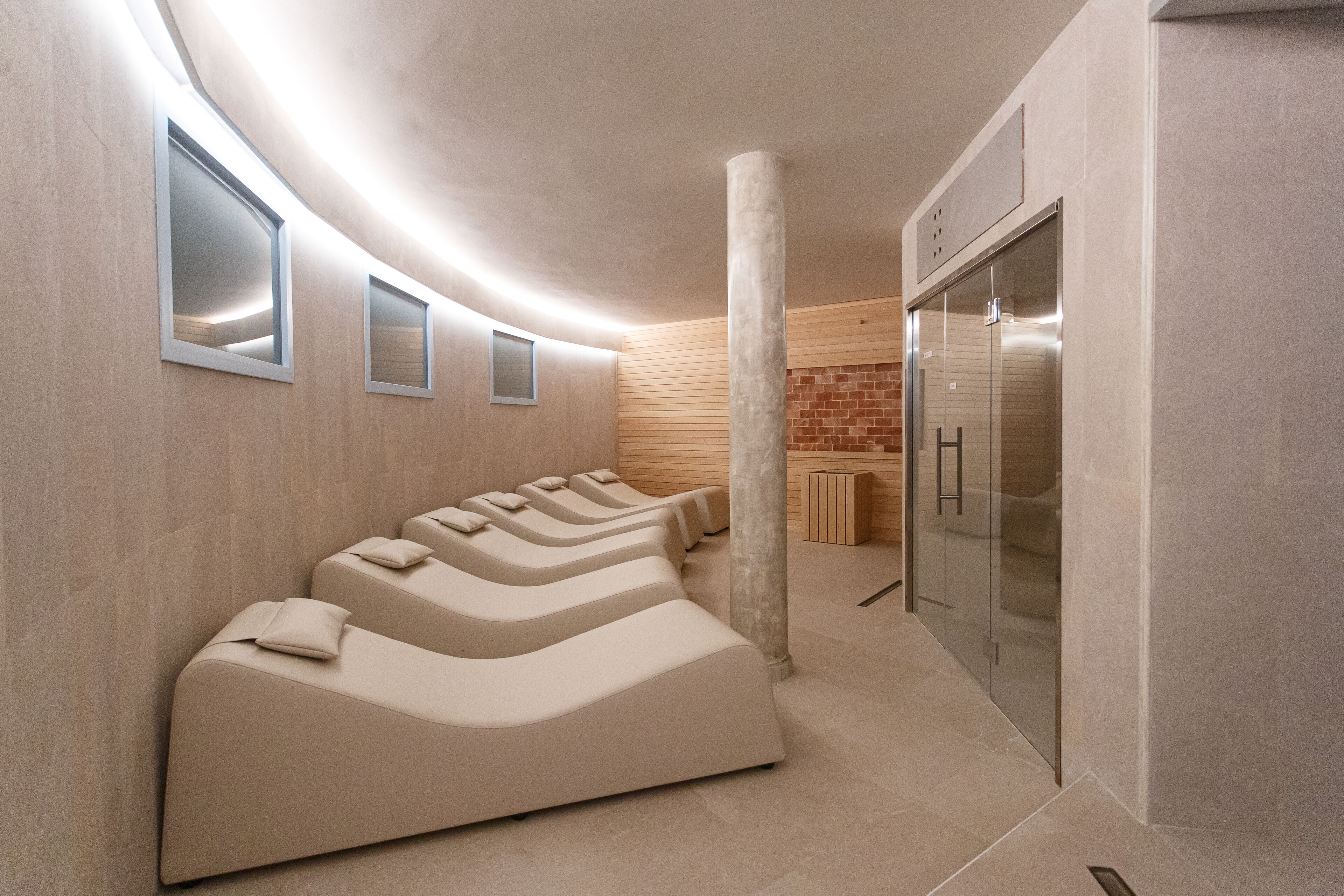 Um spa moderno com várias cadeiras de massagem, um elevador de vidro e uma parede de tijolos.