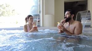 Two people in a hot tub with a view of a building and trees outside. - Oasi Blu Sardinia (Pula)