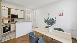 A modern kitchen with white cabinets, a microwave, and a stove. There is a dining table with two chairs and a vase of flowers. - Big spacious central apartment in Vienna (Vienna)