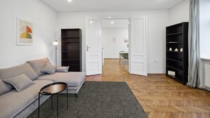 A modern living room with a grey sofa, a small round table, a bookshelf, and a door leading to a dining area. - Big spacious central apartment in Vienna (Vienna)