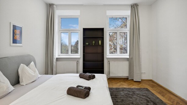 A hotel room with a bed, grey sofa, and a black shelving unit against a window. - Big spacious central apartment in Vienna (Vienna)