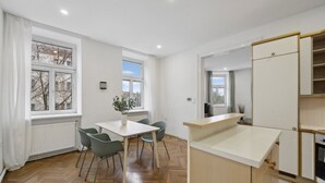 A modern kitchen with a wooden herringbone floor, a dining area with a table and chairs, and a large window providing natural light. - Big spacious central apartment in Vienna (Vienna)