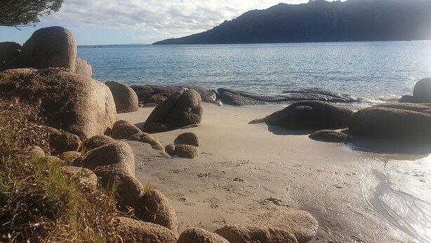 Ein Strand mit großen Felsen und freiem Blick auf das Meer.