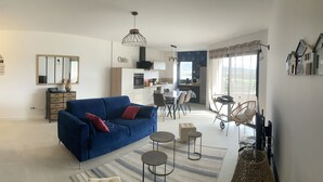Ein Wohnzimmer mit blauem Sofa, einem Essbereich, einer Küche und einem großen Fenster mit Vorhängen.