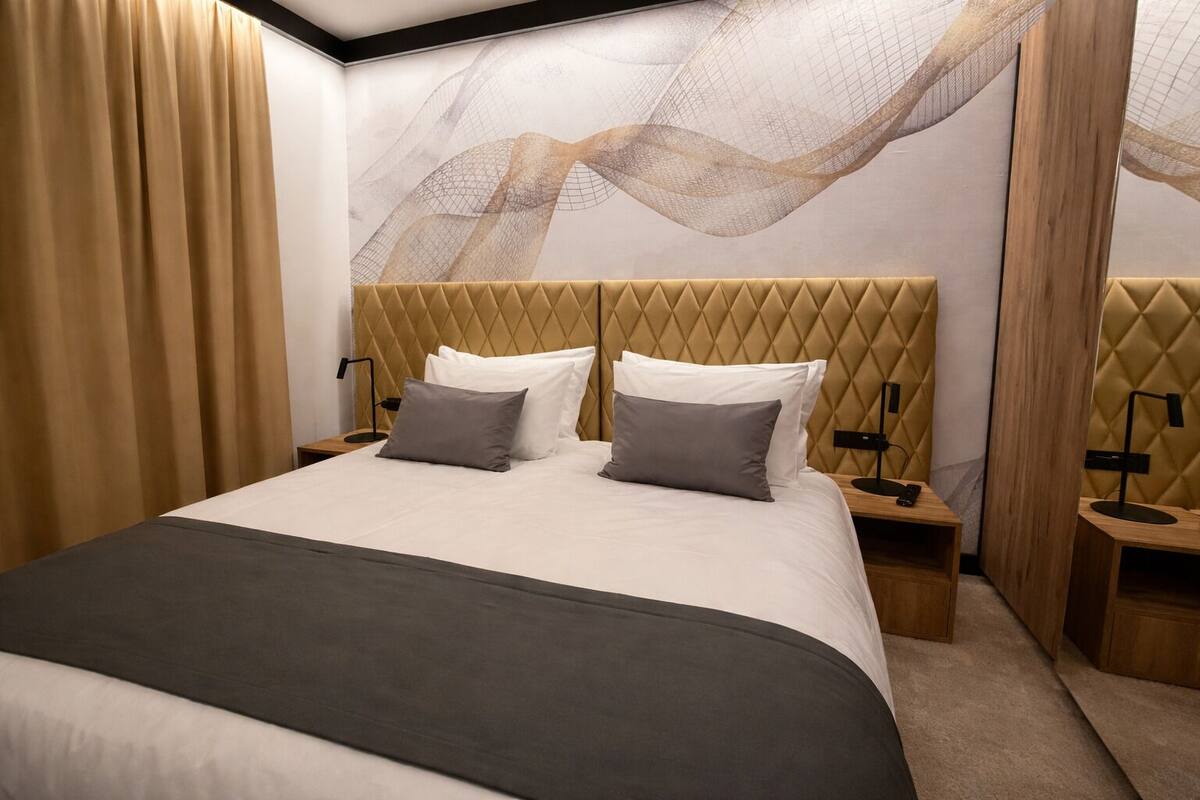A modern hotel room with a large bed, two bedside tables, and a wall mural.