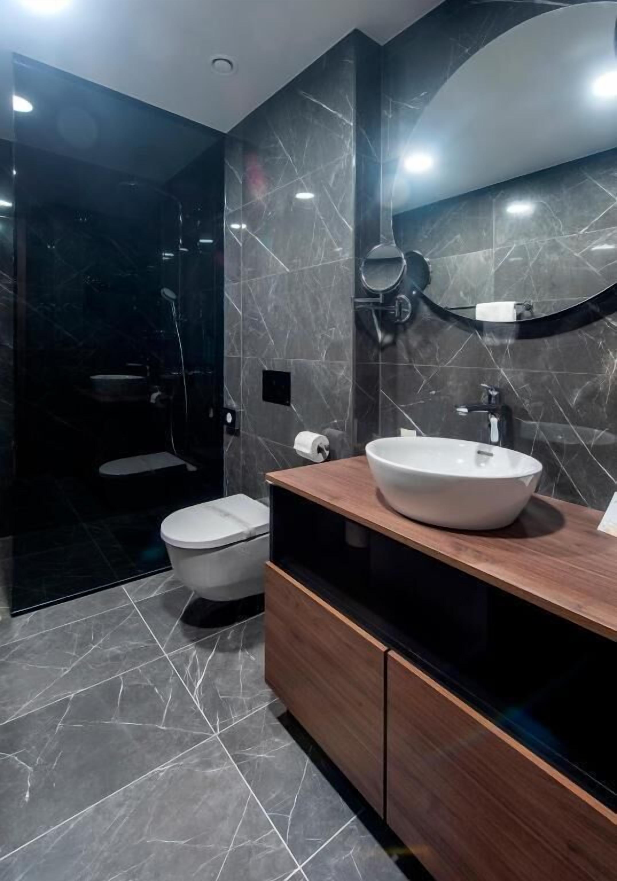 A modern bathroom with a white toilet, a large mirror, and a wooden vanity with a white sink.