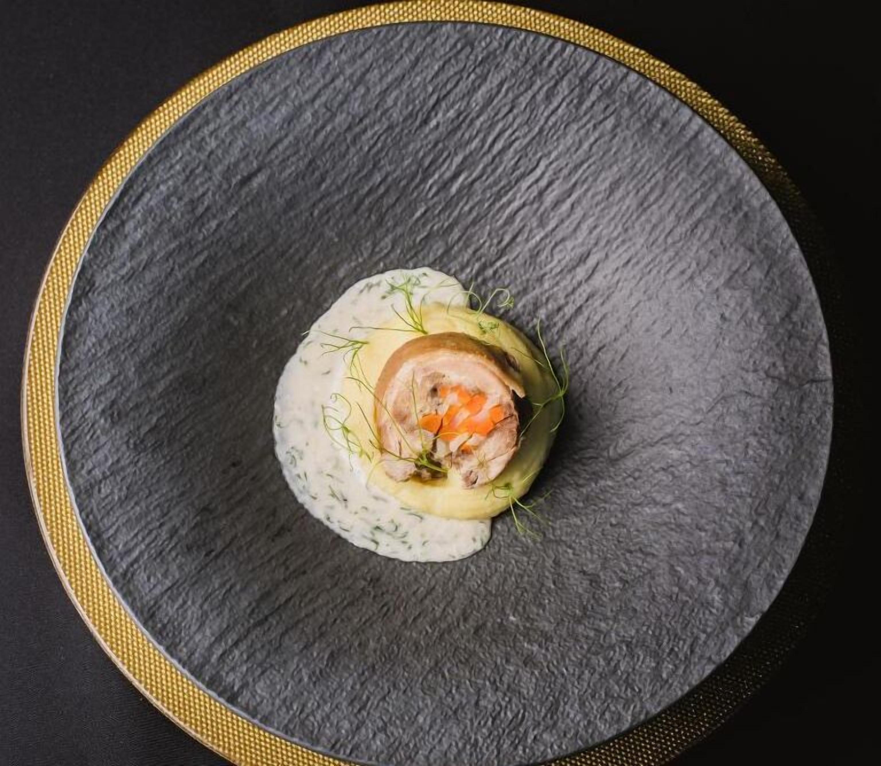 A round, dark slate plate with a golden rim, containing a food item garnished with green herbs.