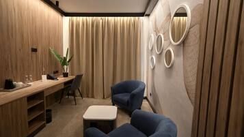 Una habitación de hotel moderna con un escritorio de madera, dos sillones azules, una mesita y una pared con espejos circulares.