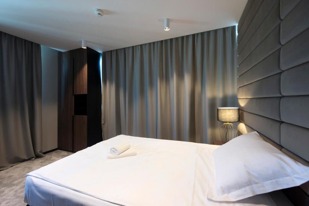 Una habitación de hotel con una cama bien hecha, una lámpara de noche y un ventanal con cortinas.