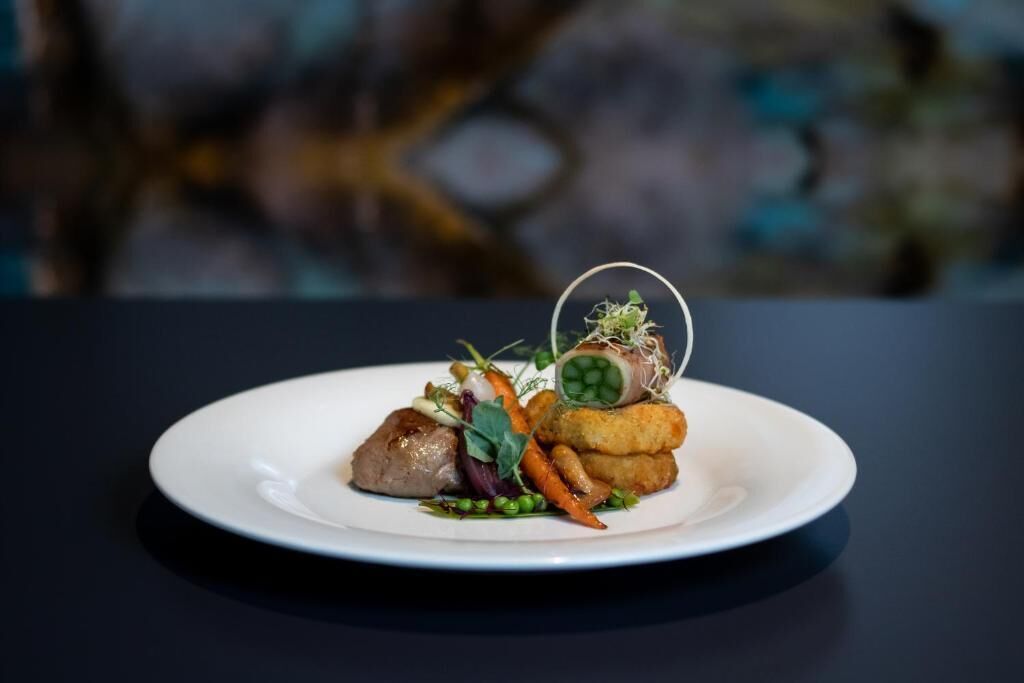 A plate of food with a piece of meat, vegetables, and a decorative element on a dark table.