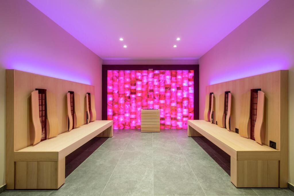 A modern spa room with wooden benches and a pink light wall.