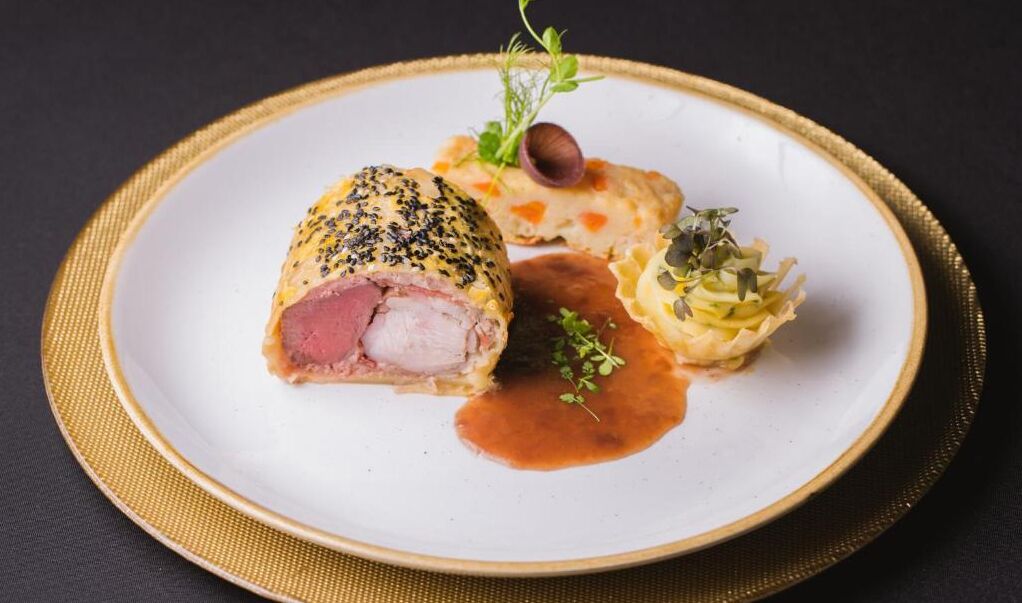 Un plato con un rollo de carne relleno, una tartaleta pequeña y una salsa.