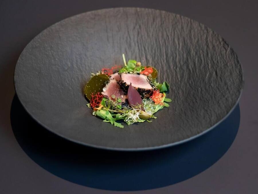 Ein schwarzer Teller mit einer Portion Essen, darunter Fleischscheiben und verschiedene Gemüsesorten.