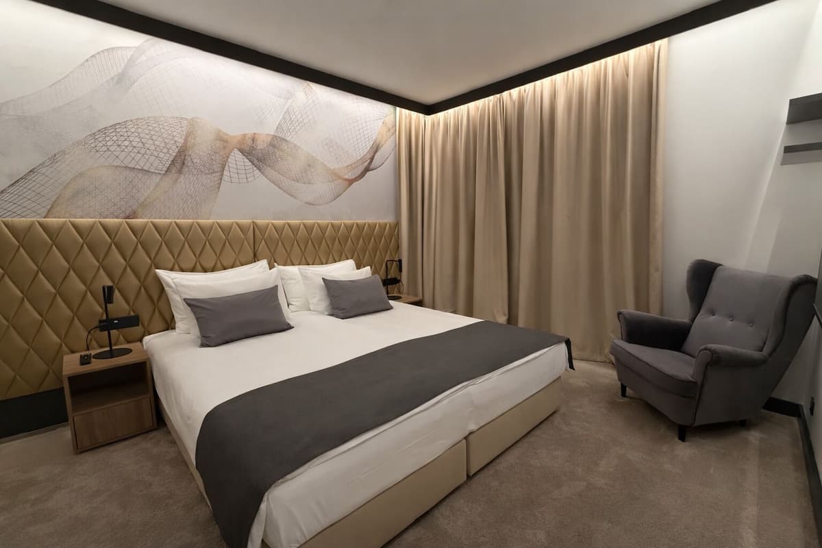 A modern hotel room with a large bed, a chair, a nightstand, and a wall with abstract art.