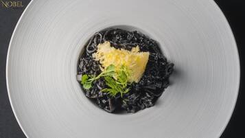 Un plato de risotto negro adornado con queso y verduras de hoja verde.