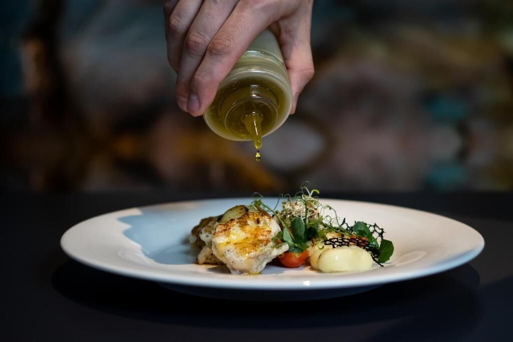 A hand pouring olive oil over a dish on a plate.