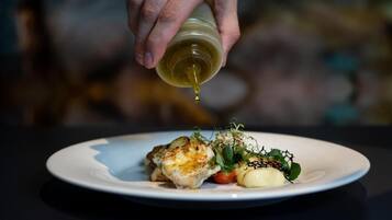 A hand pouring olive oil over a dish on a plate.