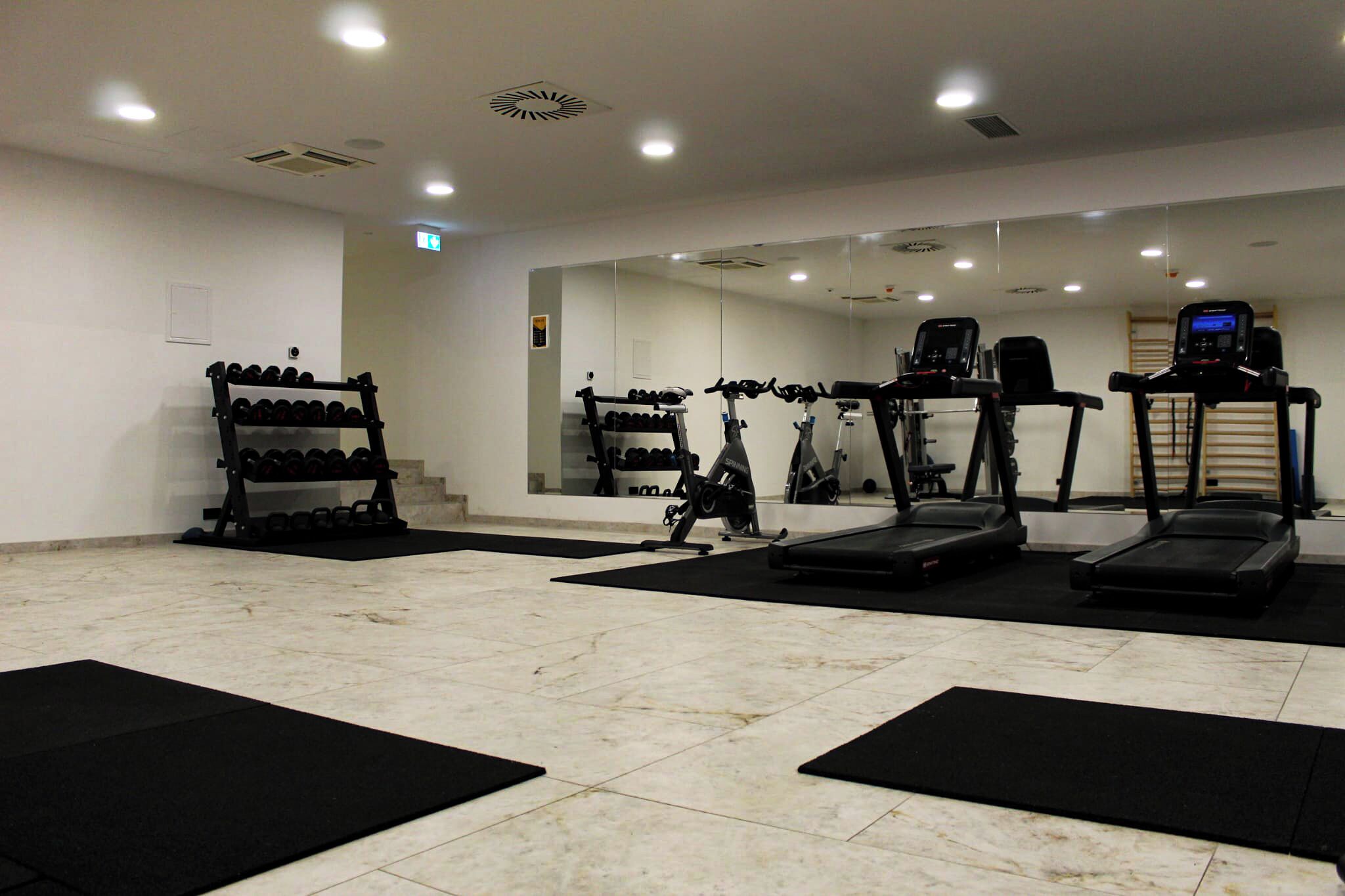 Un gimnasio con cintas de correr, bicicletas estáticas y un estante con mancuernas.