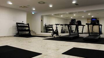 Un gimnasio con cintas de correr, bicicletas estáticas y un estante con mancuernas.
