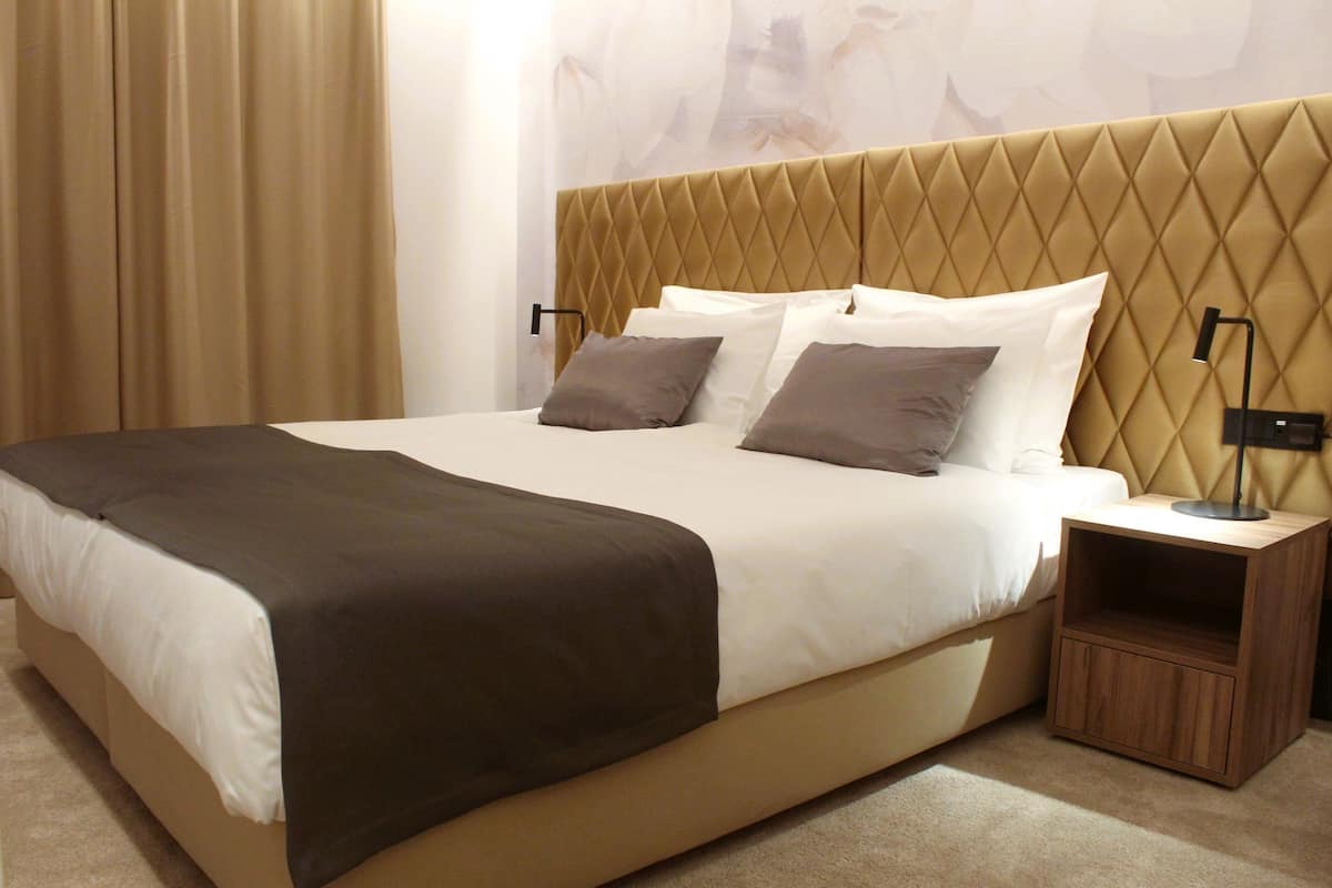 A hotel room with a large bed, two bedside tables, and a headboard with a diamond pattern.