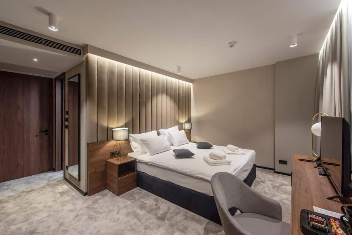 A modern hotel room with a large bed, bedside tables, a desk with a chair, and a TV.