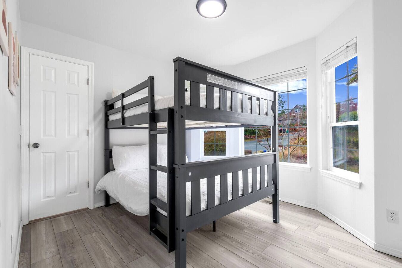 Une chambre avec un lit superposé, des murs blancs, une porte et de grandes fenêtres.