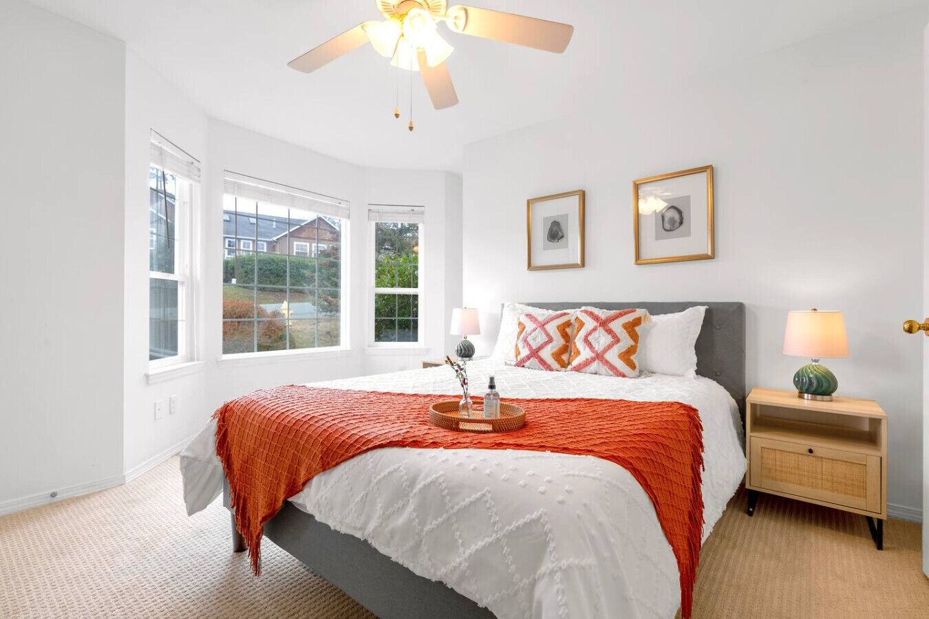 Une chambre à coucher avec un lit, deux tables de chevet, un ventilateur de plafond et de grandes fenêtres.