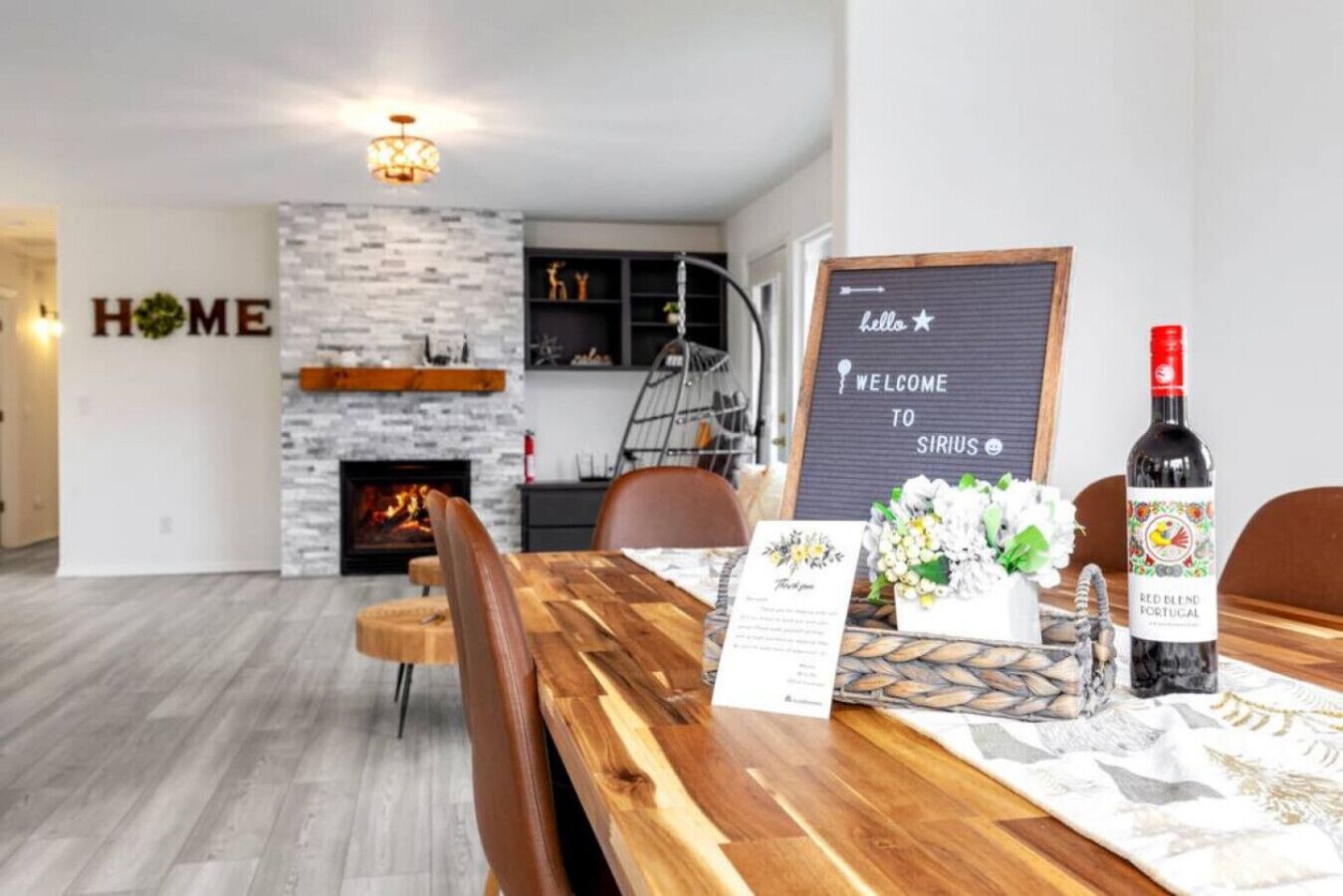 A modern living room with a fireplace, a dining area with a wooden table, and a sign that reads "hello welcome to sirius."